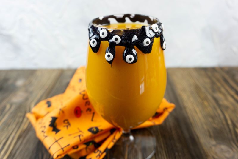 Have a little Halloween fun with this flavorful Hocus Pocus Cocktail. Made with pumpkin puree, pumpkin vodka, and orange juice! a close up photo of Hocus Pocus Pumpkin vodka cocktail decorated with edible black glitter gel and candy eyes
