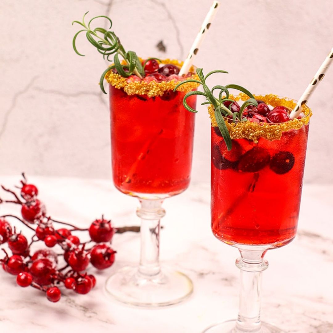 a close up photo of tow cranberry mimosas with cranberries and rosemary