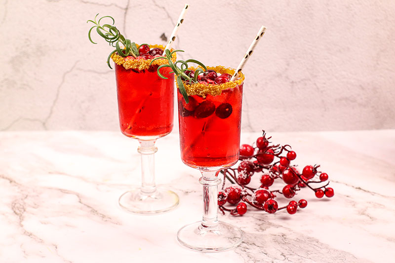 Two cranberry mimosas garnished with cranberries and rosemary