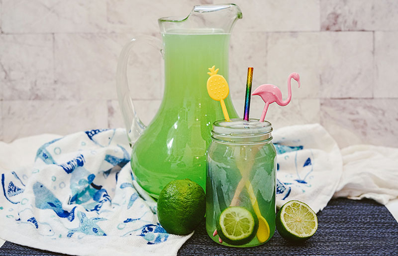mermaid water cocktail next to a big jug of mermaid water and limes 